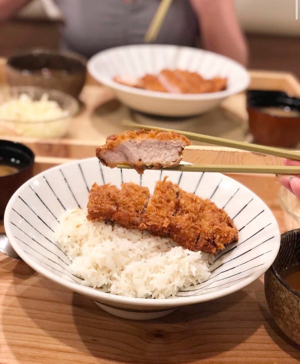 A katsu rice bowl held up with chopsticks